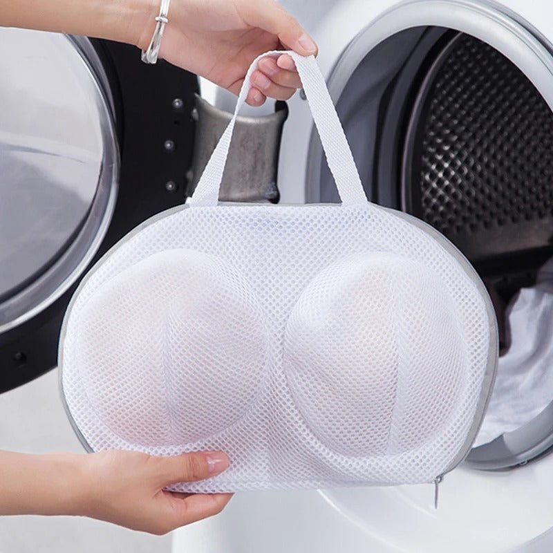 Person holding a white mesh bra bag in front of a washing machine.
